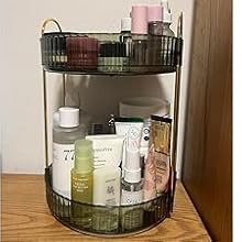 Two-tier dark metal bathroom organizer on wooden surface. Holds various personal care products and cosmetics on circular trays.