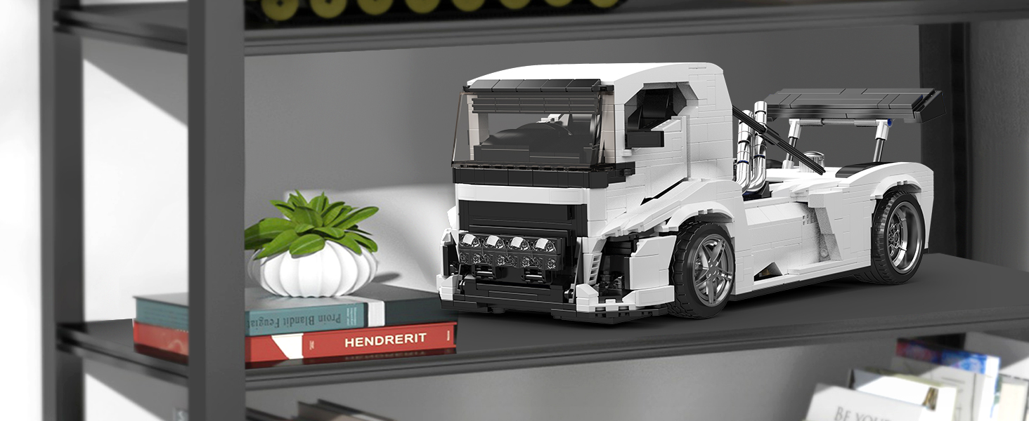White model truck displayed on dark shelf with decorative plant and red accent piece, showing detailed construction and mechanical elements.