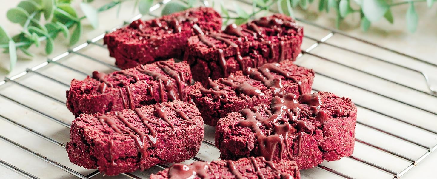Red velvet cookies or cake pieces on a wire cooling rack. The treats have a crumbly texture and deep red color, with some drizzled icing visible.