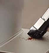 una mano que usa un cepillo para sacar los granos de café de una bandeja de metal.