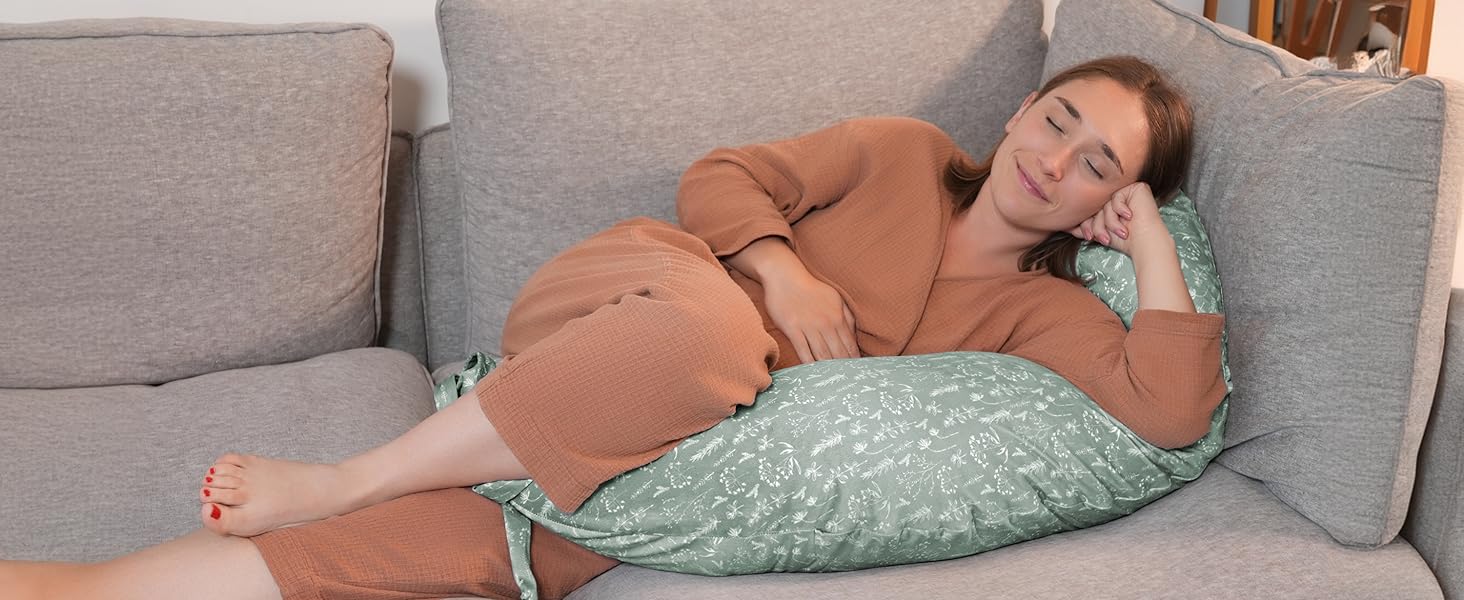 Someone resting on a grey sectional couch with a decorative mint green cushion, wearing a terracotta-colored sweater.