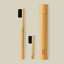 Tres cepillos de dientes de bambú con cerdas negras y una funda cilíndrica de bambú. Los cepillos de dientes varían en tamaño, y los más pequeños son aptos para viajes.