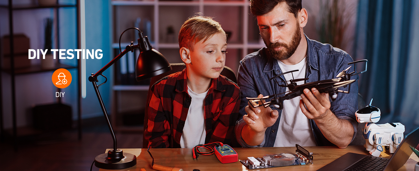 Adult and child examining a small drone or remote-controlled aircraft on a desk. Scene includes a desk lamp, suggesting a home or workshop setting for DIY projects.