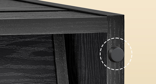 Detailný záber na roh čiernej drevenej skrinky s textúrovanou štruktúrou dreva. Viditeľná je okrúhla čierna úchytka alebo kľučka zvýraznená bielym bodkovaným kruhovým obrysom.
