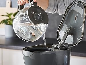 Clear liquid being poured from measuring cup into black appliance or container on kitchen counter.