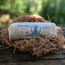 Tronco cilíndrico de queso blanco sobre superficie natural. La etiqueta es parcialmente visible pero el texto no es claramente legible.