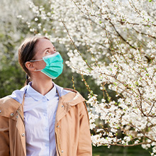 Nature's Jeannie. Woman with face mask next to tree, seasonal allergies.