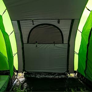 Vista interior de una tienda de campaña iluminada con luz verde, que muestra la puerta central y los compartimentos contiguos