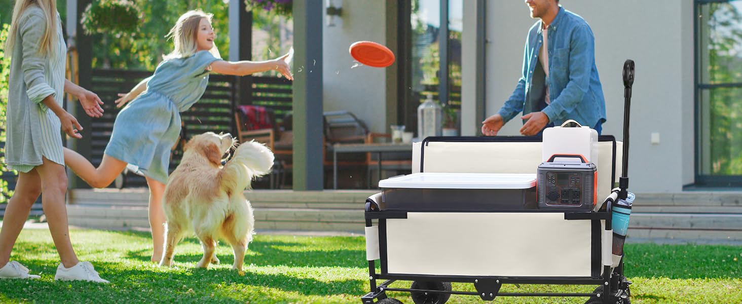Collapsible outdoor utility wagon with large wheels on grass. People playing frisbee and walking dog nearby. Wagon features white fabric sides and black frame.