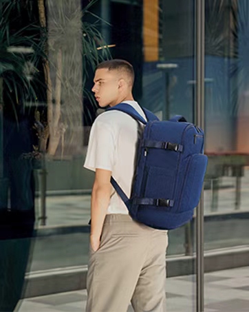 Una persona che indossa un abbigliamento casual con pantaloni cachi e camicia bianca, con uno zaino blu marino, in piedi davanti a una vetrina di vetro.