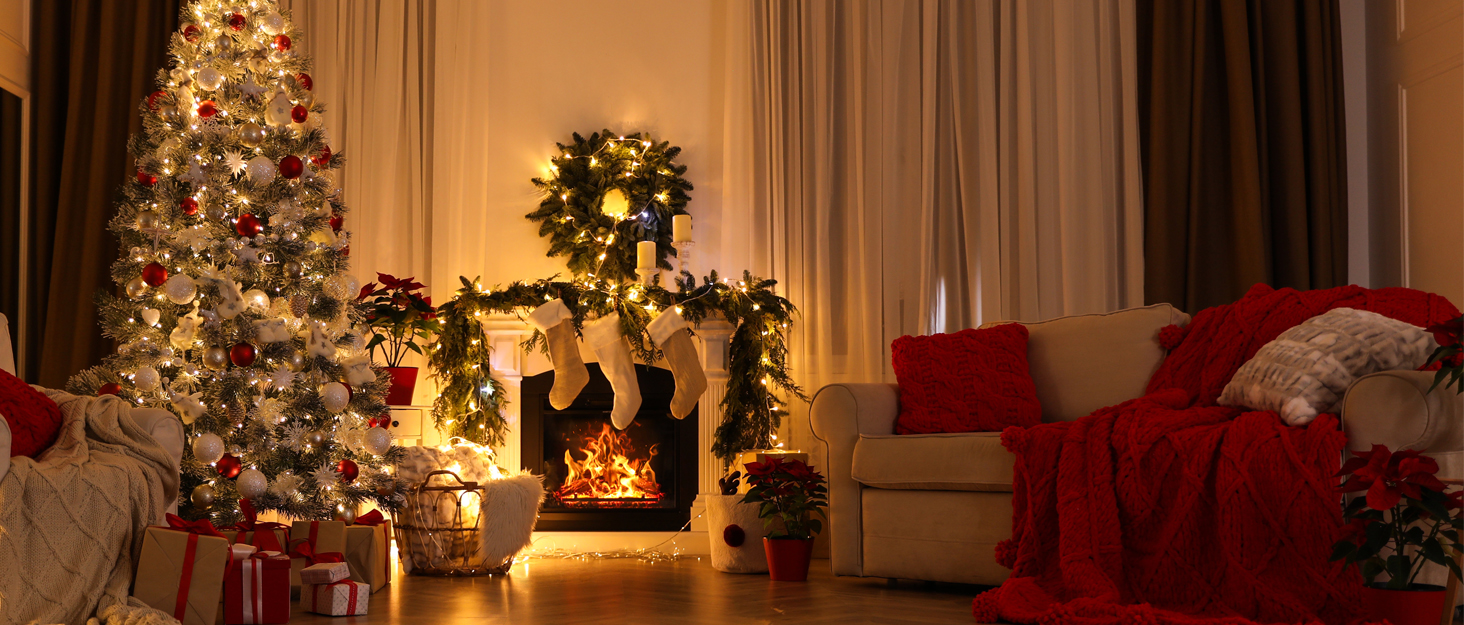 Cozy living room decorated for Christmas with lit tree, fireplace, red couch, and warm ambient lighting creating festive atmosphere.