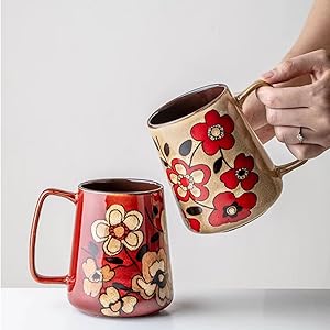 Two ceramic mugs featuring floral designs - one in beige with red flowers, one in burgundy with light-colored flowers, both with sturdy handles.