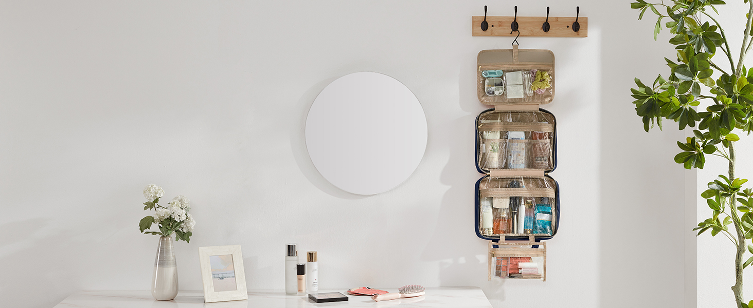 Wall-mounted organizer with multiple fabric pockets, hanging next to a round mirror in a bright, minimalist interior setting with plants and decor.