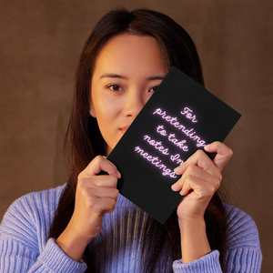 woman holding a black and neon coloured notebook in front of her face