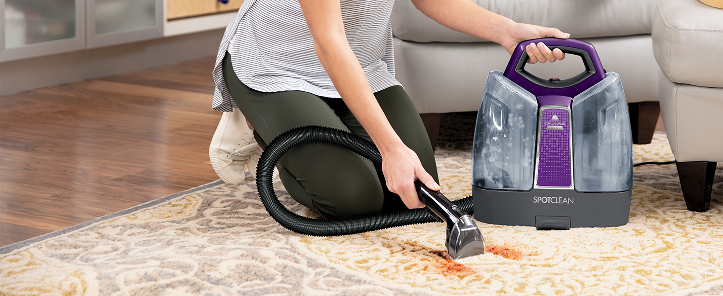 Bissell SpotClean being used on a rug to clean up a red stain.