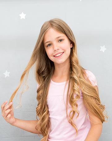 Jeune fille aux longs cheveux blonds ondulés portant un t-shirt rose clair. Fond gris avec décorations d'étoiles blanches.