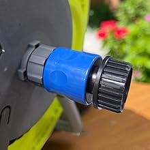 Close-up of a black and lime green device with blue rotating connector or adjustment knob visible against blurred garden background.
