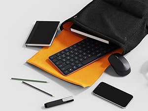 Black bag contents displaying mobile accessories including wireless keyboard, mouse, mobile device, and writing implements on white background.