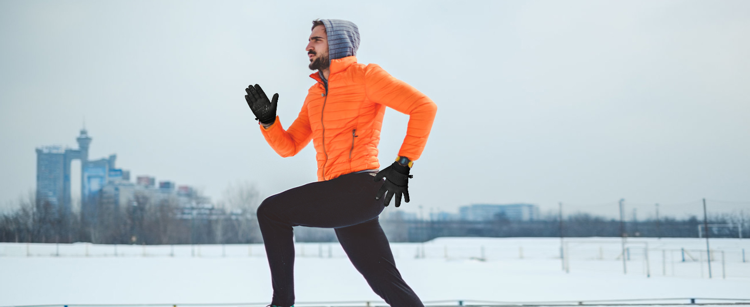 Person jogging in snowy landscape wearing bright orange jacket, black pants, gloves, and grey hood.