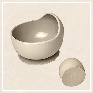 Two light-colored ceramic pieces: a larger asymmetrical bowl with curved sides and a smaller spherical object, possibly a lid, on a neutral background.