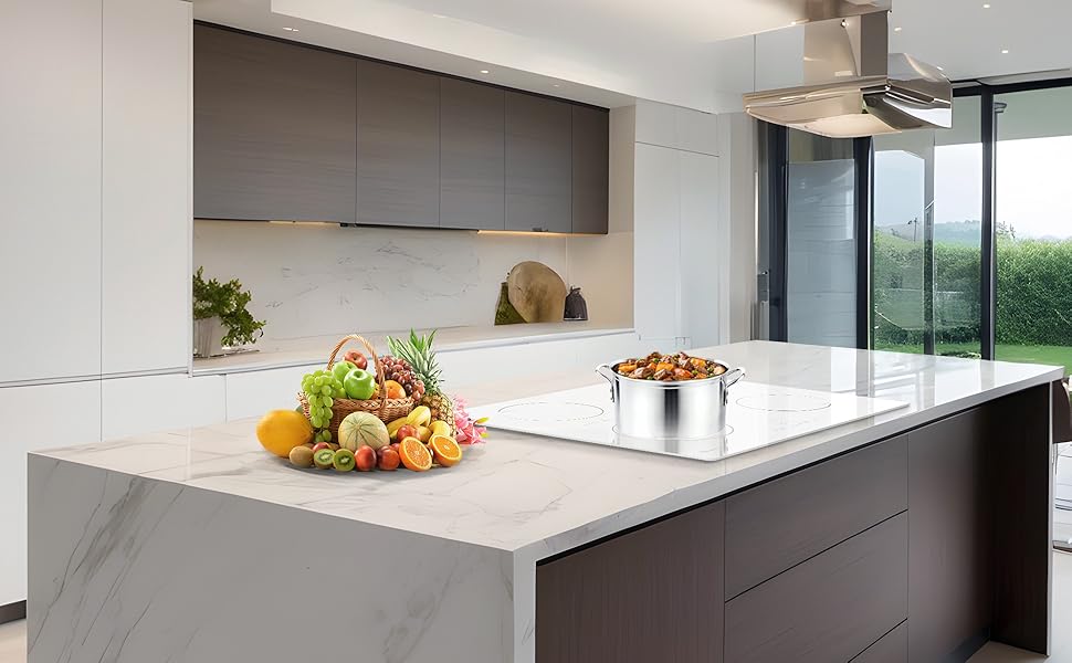 Modern kitchen with white countertop island. Fresh produce displayed. Stainless steel pot on counter. Large windows with outdoor view.