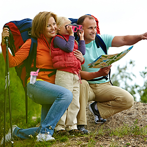 Two hikers with backpacks sitting outdoors. One points off-camera while the other consults a map, suggesting they're planning a route or identifying landmarks.