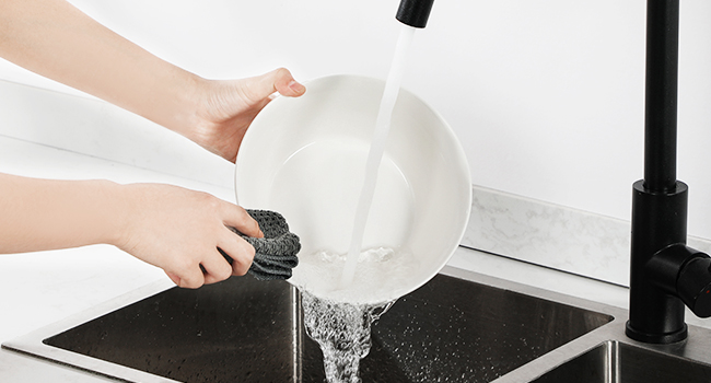a woman is washing dishes in a bowl with soap.