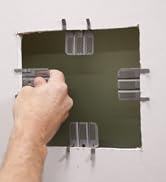 4 WAL-BOARD TOOLS Drywall clips, one on each side of a square hole in a section of drywall