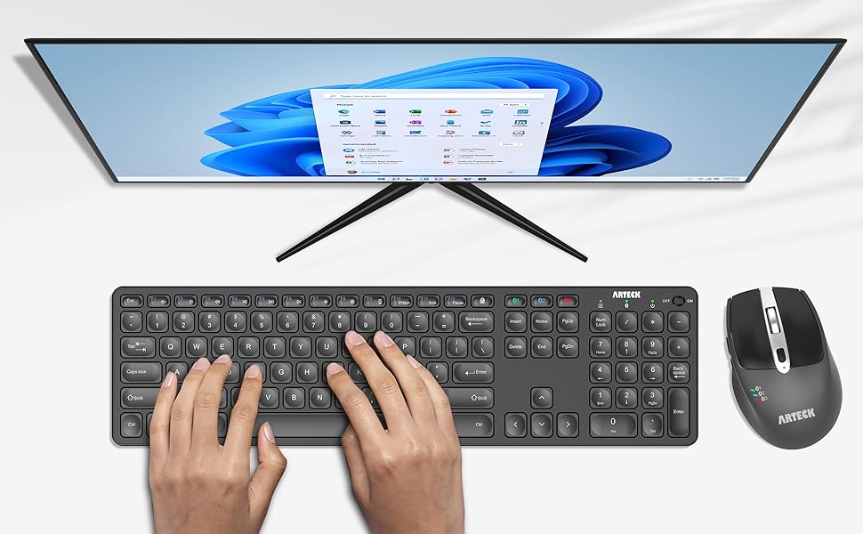 Computer setup showing a widescreen monitor displaying blue graphics, with a full-size wireless keyboard and mouse. Keyboard shown in active use position.