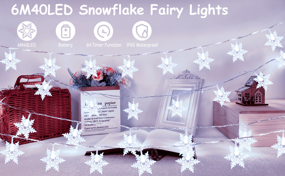 String of LED snowflake-shaped fairy lights illuminating a room with decorative elements. Product features listed: 6M, 40LED, battery-operated.