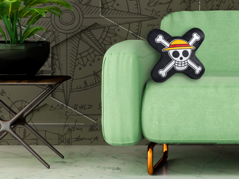 Decorative skull and crossbones pillow on light green couch. Black pillow features white skull design with yellow details.