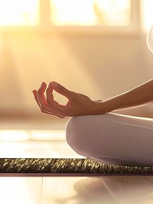 Person sitting in lotus position on yoga mat, hands in meditation mudra, backlit by warm sunlight through windows.
