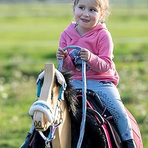 Reitszene im Freien mit einem Pony mit blauer und rosa Zaumzeugausrüstung auf einer sonnigen grünen Wiese.