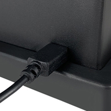 Primer plano de un dispositivo electrónico negro con un cable de alimentación enchufado en un lateral, sobre un fondo blanco