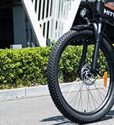 Primer plano de la rueda delantera de una bicicleta con un neumático con nudos, lo que sugiere que está diseñada para uso fuera de carretera. Vista parcial del cuadro y la horquilla visibles