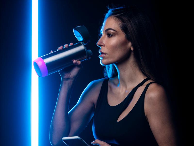 A woman in workout clothes drinks from a Hidrate STEEL bottle with a chug lid
