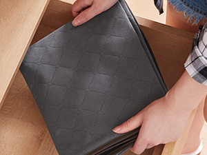 Hände legen eine dunkelgraue gesteppte Schaumstoffmatte in eine Holzschublade. Die Matte scheint eine gepolsterte Einlage oder ein Schubladenfach mit strukturierter Oberfläche