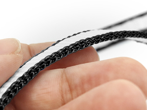 Close-up of fingers holding a thin, black braided cable or cord against a white background. The cable has a textured, woven appearance.