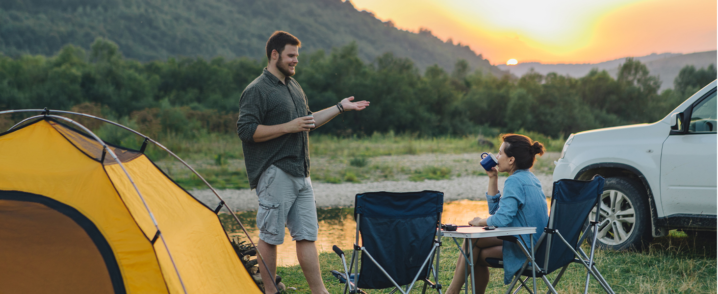 Outdoor camping scene at sunset. Man and woman sitting by tent and vehicle. Mountainous background.