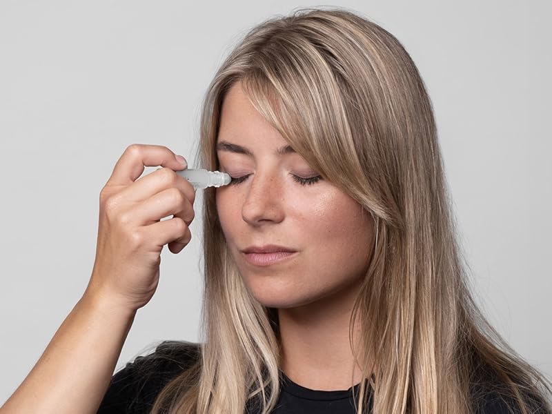 Close-up of a person applying a small white device to their closed eye, possibly an eye massager or treatment tool.