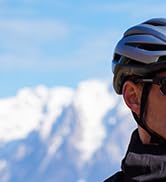 Partial view of a person wearing a blue cycling helmet against a snowy mountain backdrop.