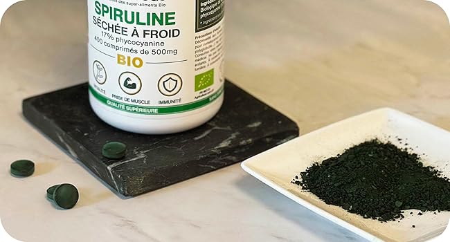Flacon de supplément de spiruline biologique sur une surface en pierre noire avec de la poudre verte affichée sur une plaque blanche à côté des comprimés
