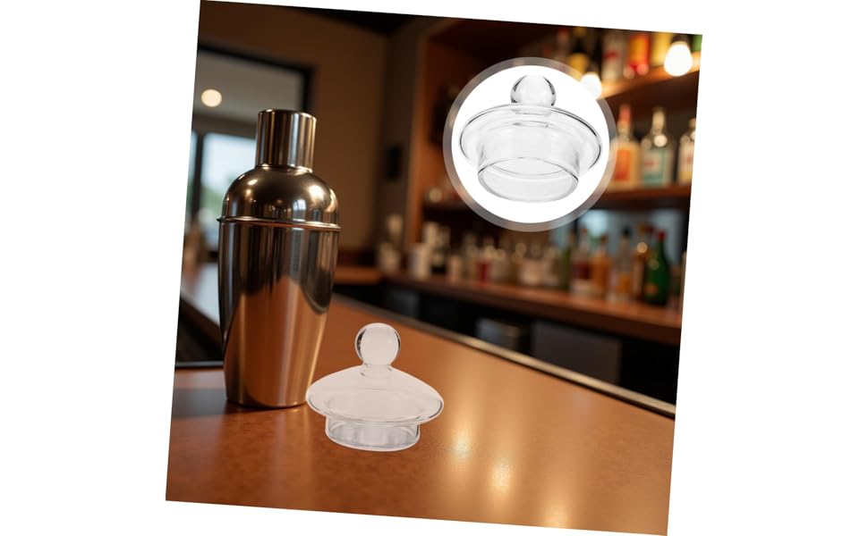 Bar setting with metal cocktail shaker and bottle stopper or pour spout on wooden counter surface.