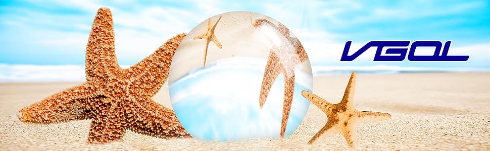 Clear glass sphere on sandy beach with starfish. Reflects blue sky and clouds. Large starfish beside sphere, smaller one visible through glass. Brand name 'VISOL' in blue text.