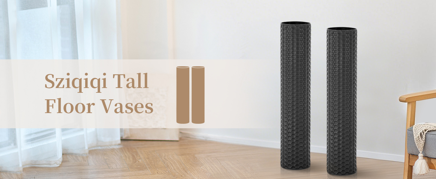 Two tall cylindrical floor vases with textured black surfaces. The vases are slender and stand prominently in a minimalist room setting with wooden flooring.