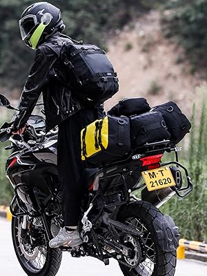 Motorcyclist on adventure bike with black and yellow luggage bags. Rider wears black gear with neon accents. Bike has off-road tires and rugged appearance for long-distance travel.