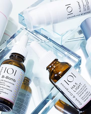 Collection of skincare products including bottles and vials in white, blue, and amber colors, arranged on a reflective surface.