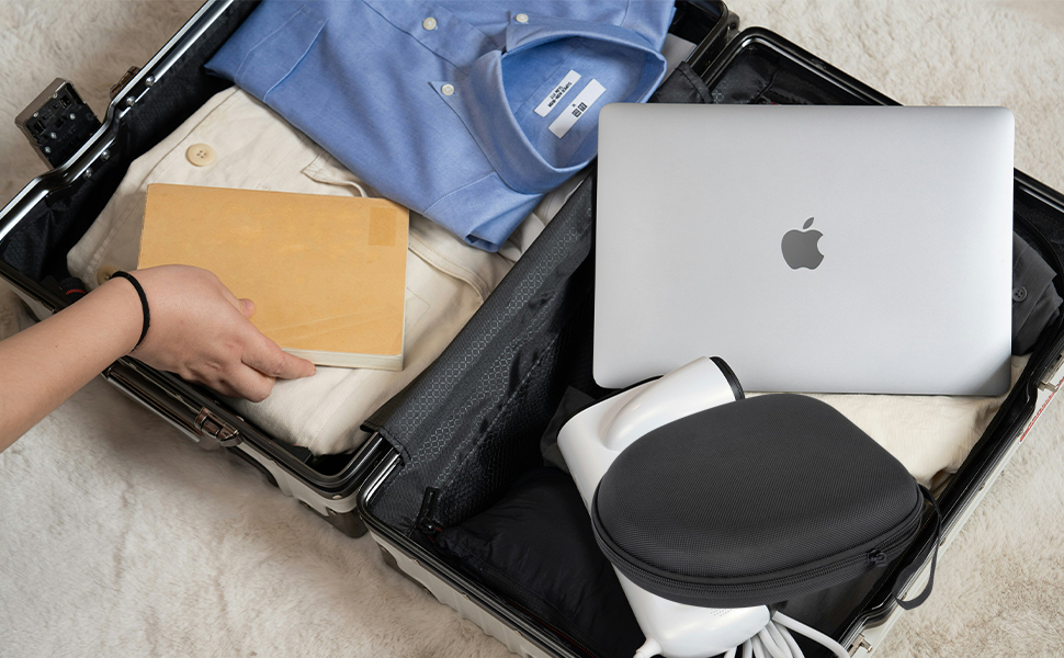 Open suitcase containing clothing, laptop, headphones, and other travel essentials. Hand placing a folder into the luggage, showcasing efficient packing for a trip.