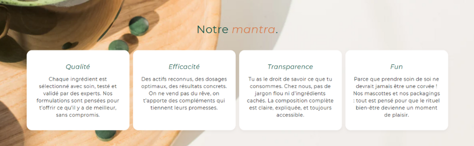 Quatre cartes de visite sur une surface en bois affichant les valeurs de l'entreprise : qualité, efficacité, transparence et divertissement. Le texte est en français. Vue partielle d'une main et d'une plante en arrière-plan.