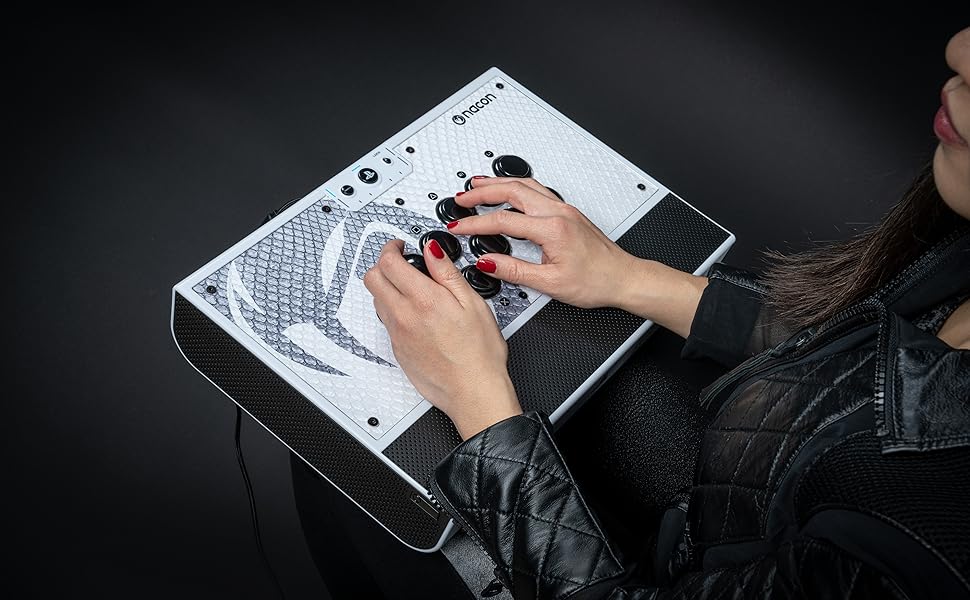 Les mains actionnent un appareil électronique rectangulaire blanc doté de commandes et de boutons circulaires. L'appareil semble être un contrôleur audio ou musical spécialisé.